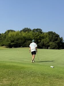 青空の下でbattingaTシャツを着てゴルフをする男性の後ろ姿